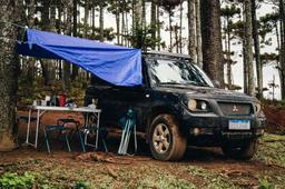 Mørk SUV med blå presenning rigget som markise, campingbord og stoler