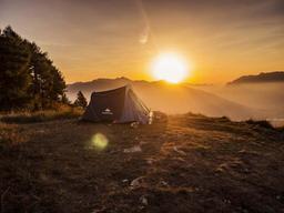 Kuppeltelt på en fjellrygg med sola rett bak