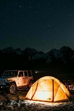 Jeep ved siden av et glødende oransje telt under stjernehimmel