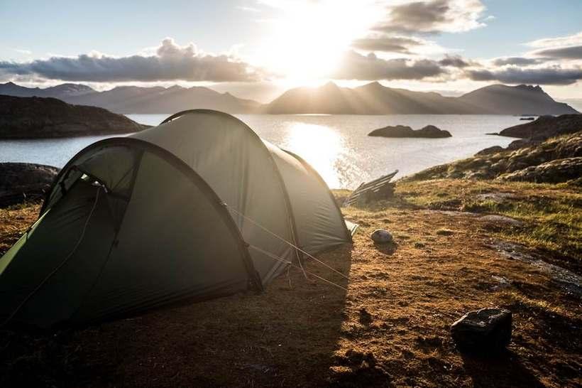 Mørkegrønt tunneltelt satt opp på en klippekant med utsikt over en norsk fjord i lavt kveldslys