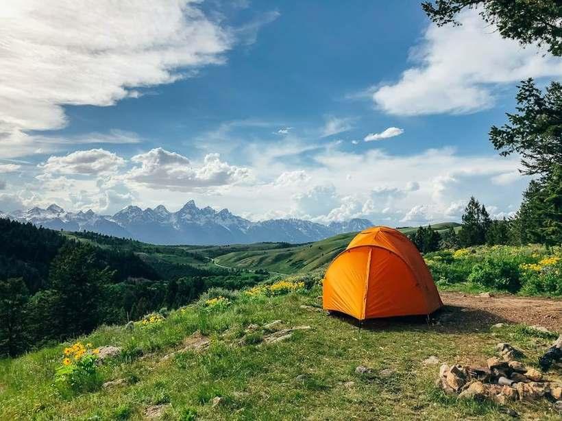 Oransje kuppeltelt satt opp på en grønn fjellside med blå himmel
