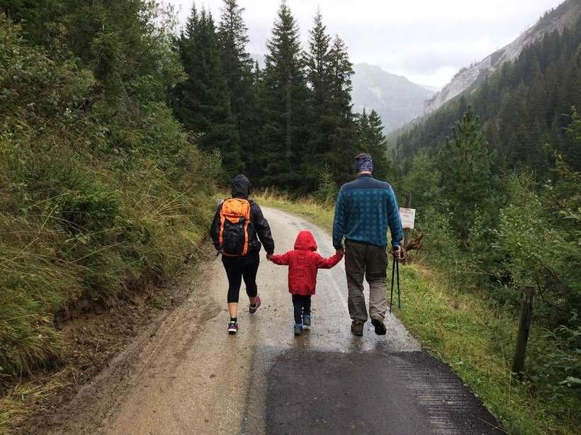 To voksne og et lite barn går hånd i hånd nedover en grusvei i skogen