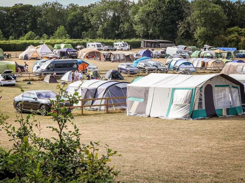 Campingplass sett ovenfra med mange store telt og parkerte biler